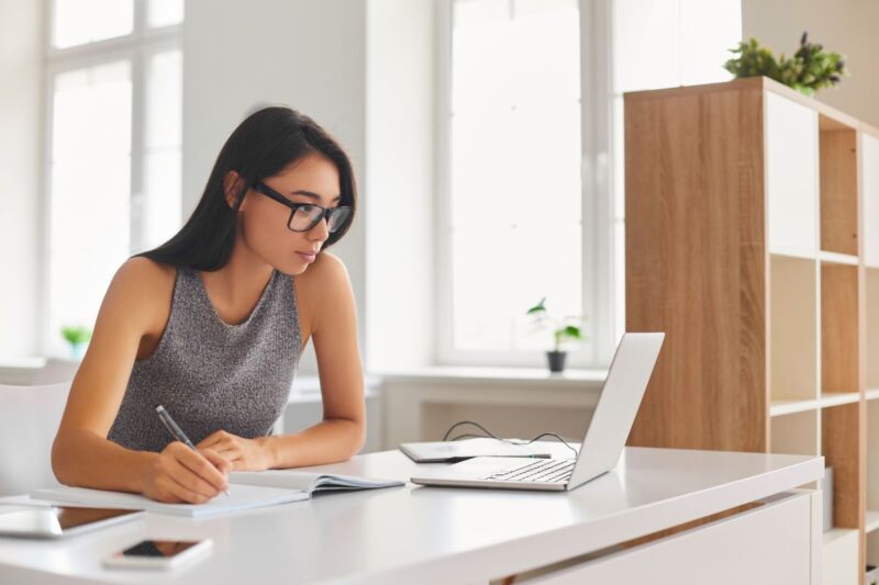 Jovem organizando finanças pessoais com laptop e caderno em casa.